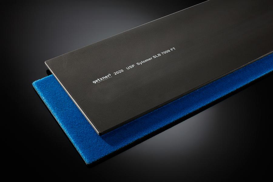 Eine Metallplatte in Schwarz mit eingravierten Zahlen und Begriffen, die auf einem blauen Schaumstoffuntergrund liegt. Die Platte ist flach und länglich, der Hintergrund ist dunkel und hebt die Objekte hervor.