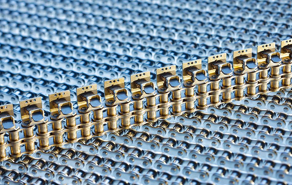 Eine Nahaufnahme von metallischen Kettenelementen auf einem blauen Hintergrund. Die Kette ist aus goldfarbenem Metall gefertigt und verläuft in gerader Linie. Die Struktur und Details der Kette sind gut sichtbar.