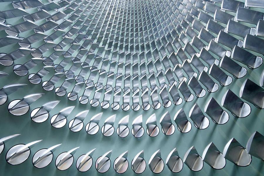 Eine abstrakte Struktur mit sich spiralförmig anordnenden, glänzenden Metallteilen. Die Elemente sind halbrund und reflektieren das Licht, was einen dynamischen Eindruck erzeugt. Der Blickwinkel ist von unten nach oben gerichtet, wodurch die Tiefe der Form betont wird.