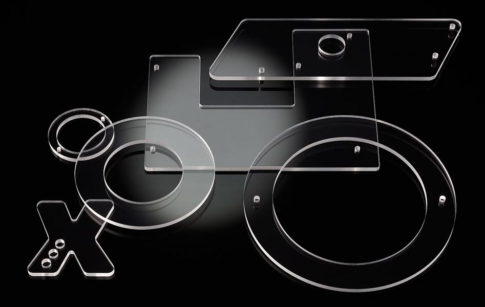 Eine Anordnung von klaren, geometrischen Formen aus Acryl, einschließlich Rechtecken, Kreisen und einem „X“. Die Formen liegen auf einer dunklen Oberfläche und reflektieren Licht, was ihre Transparenz und Struktur betont.