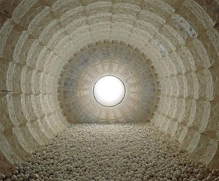 Eine Ansicht von innen in einen großen, runden Behälter, der mit vielen weißen Kugeln auf dem Boden gefüllt ist. Am oberen Ende des Behälters ist ein helles Licht sichtbar, das den Eindruck von Tiefe und Weite vermittelt.