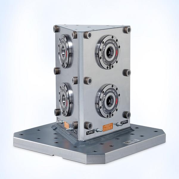 Ein quadratisches, metallisches Gerät mit vier runden Öffnungen auf den Seiten. Es steht auf einer flachen, rechteckigen Basis. Die Oberfläche ist glänzend und zeigt technische Details, einschließlich Beschriftungen wie "TURBO" und "OPEN".