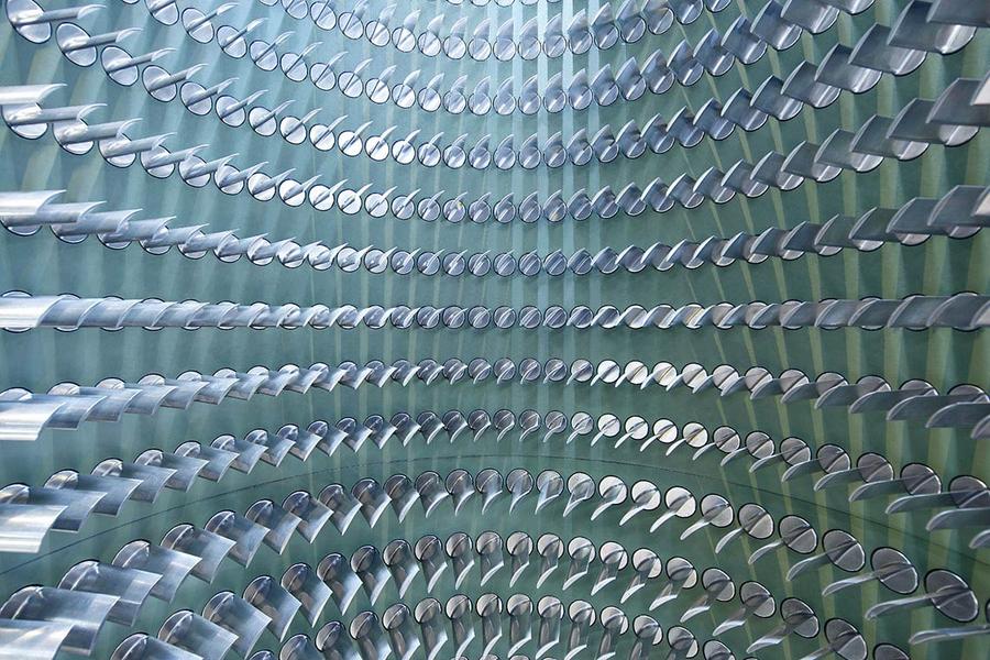 Ein Muster von vielen silbernen Rohren, die kreisförmig angeordnet sind. Die Rohre sind teilweise spiegelnd und reflektieren das Licht, was einen dreidimensionalen Effekt erzeugt. Der Hintergrund ist in einem sanften Grünton gehalten.