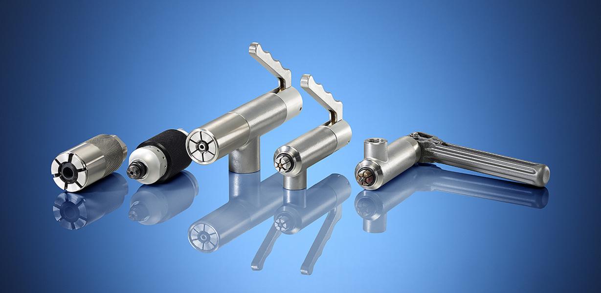 Abbildung von vier verschiedenen metallenen Werkzeugen auf einem blauen Hintergrund. Werkzeuge haben unterschiedliche Formen und Funktionen, darunter eine angepasste Griffstruktur und diverse Aufsätze.