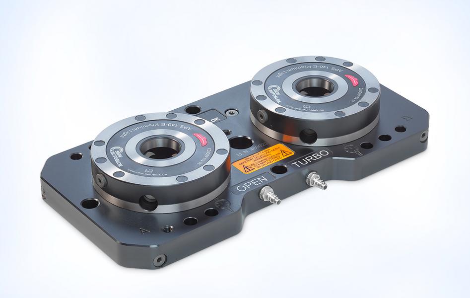 Schwarze Plattenkomponente mit zwei runden, metallischen Vorrichtungen auf der Oberseite. Jede Vorrichtung hat einen roten und silbernen Ring sowie Beschriftungen. Die Platte enthält zusätzliche Anschlüsse an der Seite, die auf technische Funktionen hinweisen.