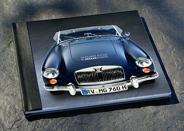 Ein graues Fotobuch liegt auf einer Oberfläche, das eine Abbildung eines klassischen blauen Autos zeigt. Auf dem Buchcover sind die Worte "Oldtimer Fotos by BEICKERSTUDIOS" zu sehen.