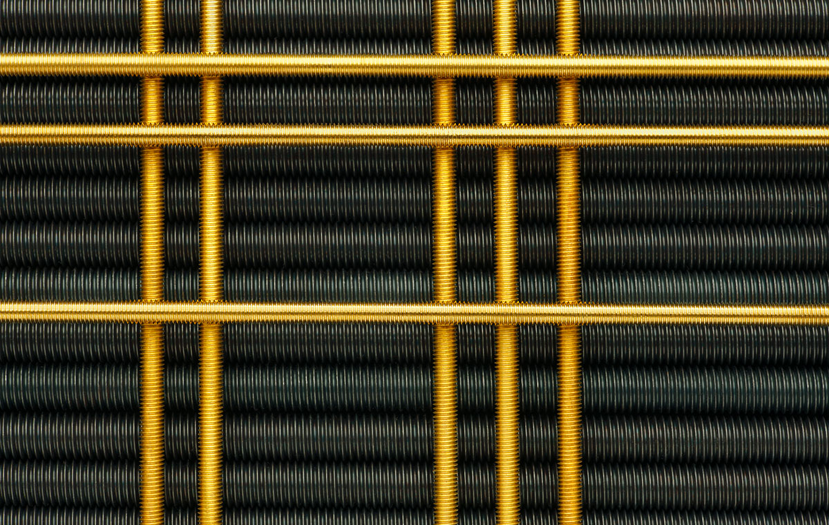 Nahaufnahme von Drahtgeflecht in schwarzer und goldener Farbe, das ein grafisches Muster bildet. Die schwarzen Drahtschlingen sind in Reihen angeordnet, während die goldenen Drähte quer verlaufen und ein strukturiertes, industrielles Design erzeugen.