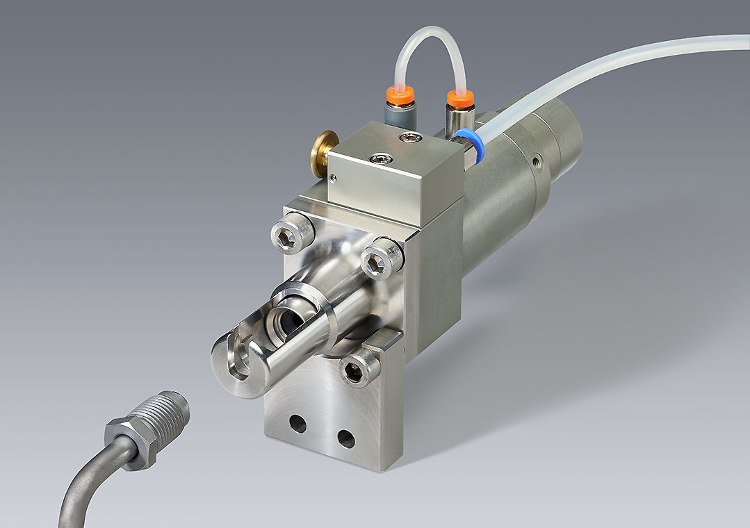 Eine präzise Maschinenteileinheit, bestehend aus einem metallischen Gehäuse mit Anschlüssen und Schläuchen. Der Fokus liegt auf dem Ventilmechanismus, der für industrielle Anwendungen eingesetzt wird. Im Hintergrund ist eine neutrale graue Fläche.
