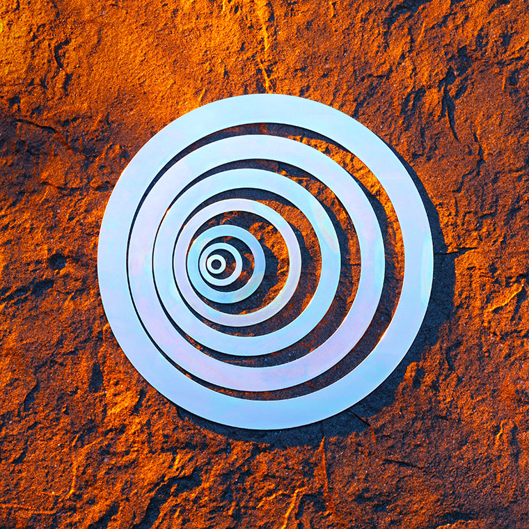Unterlegscheiben in verschiedenen Größen, das auf einer strukturierten, orangefarbenen Oberfläche platziert ist. Die Ringe sind in einem hellen, glänzenden Material gehalten, das Licht reflektiert.