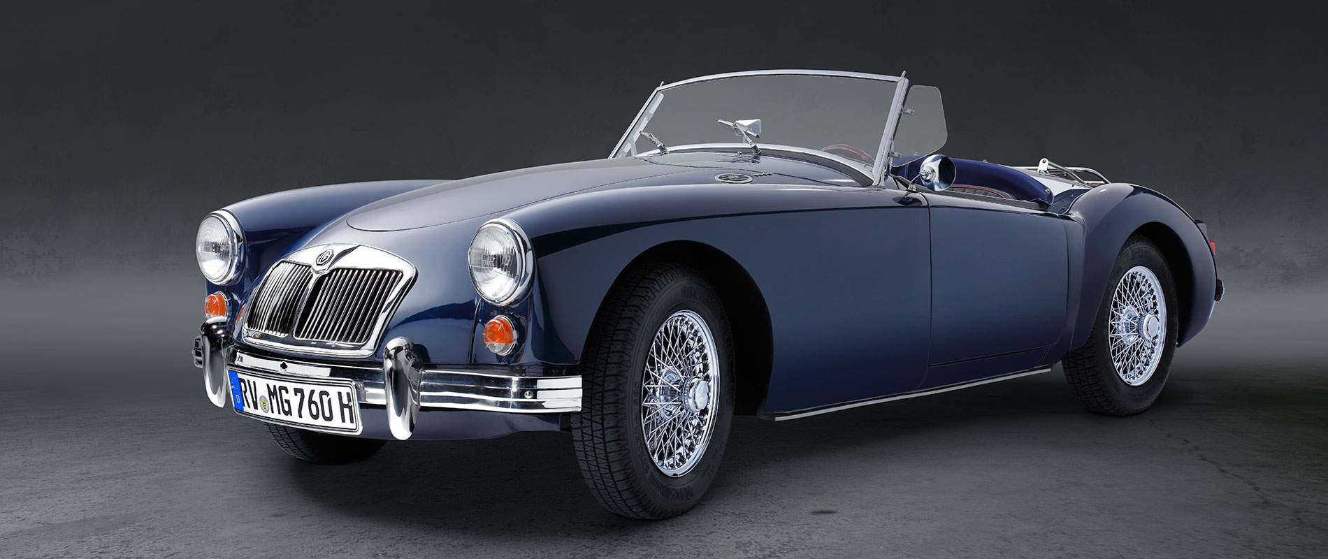 Ein blauer Sportwagen im Cabriolet-Stil steht auf einer neutralen Fläche. Das Auto hat einen klassischen Look mit verchromten Details und einem offenen Verdeck. Die Felgen sind verchromt und auffällig gestaltet.