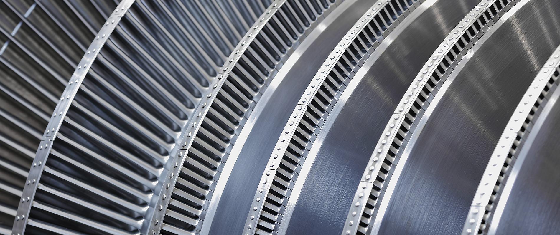 Detailaufnahme von mehreren Schaufelreihen einer Turbine. Die metallischen Oberflächen sind glatt und reflektieren das Licht, während die Schaufeln eine präzise und gleichmäßige Anordnung zeigen.