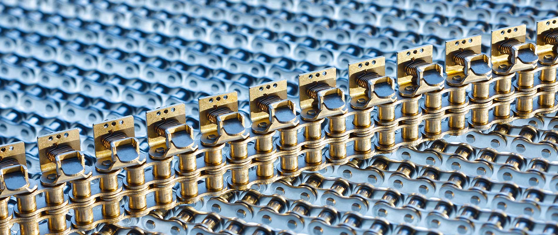 Detailaufnahme von metallischen Bauteilen, die in einer geraden Linie angeordnet sind. Die Teile haben eine goldene Farbe und sind auf einer blauen, strukturierten Fläche platziert. 